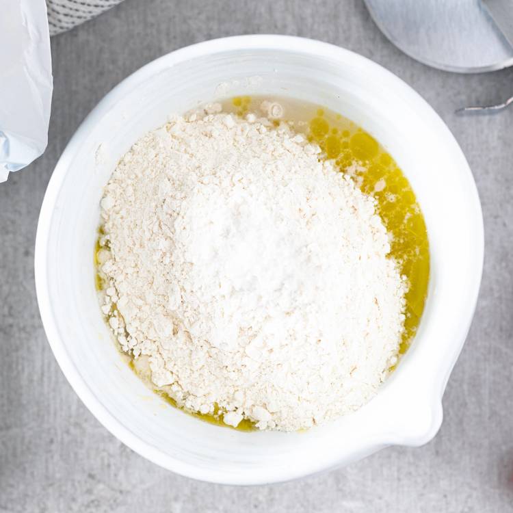 Pizzadeig med mel og olje i en stor hvit bolle på et kjøkkenbord.