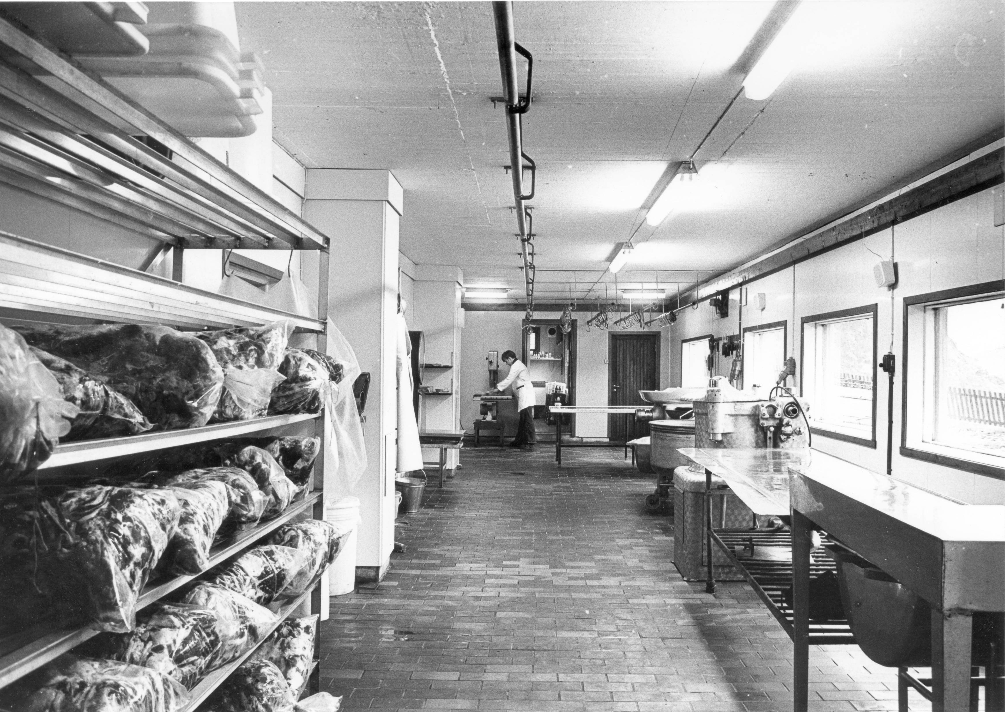 Interiør av en fabrikk med arbeidsbenker og store vinduer, hvor en person jobber i bakgrunnen.