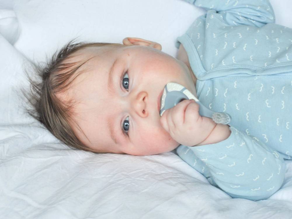 Et barn ligger i sengen med ansiktet dekket av en pappplate, iført lyseblå pysjamas med mønster av hvite måner og stjerner.