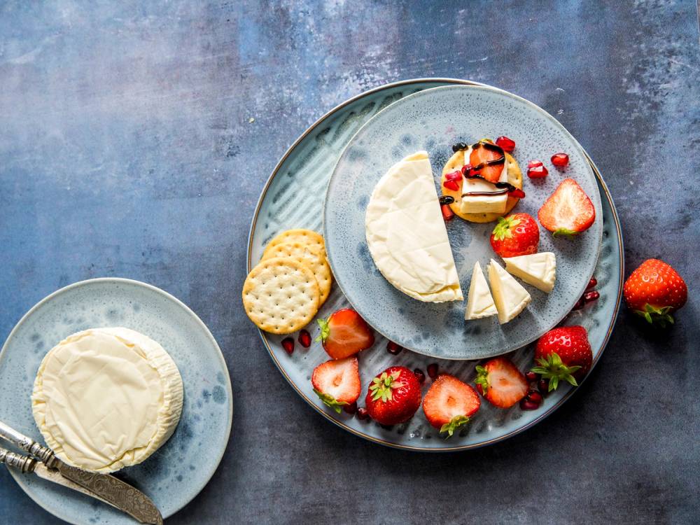 Et fat med ulike oster, friske jordbær og kjeks, med en liten tallerken med ost ved siden av.