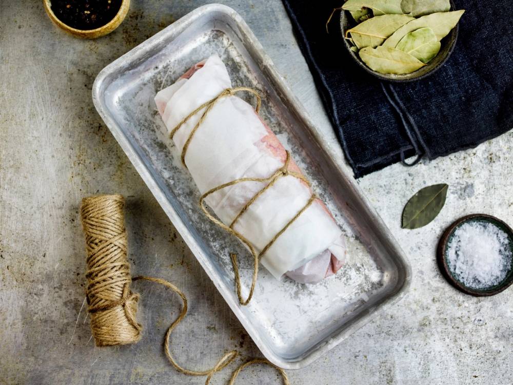Torsk med rogn pakket inn i plastfolie og bundet med hyssing i en metallform, omgitt av krydder og urter.