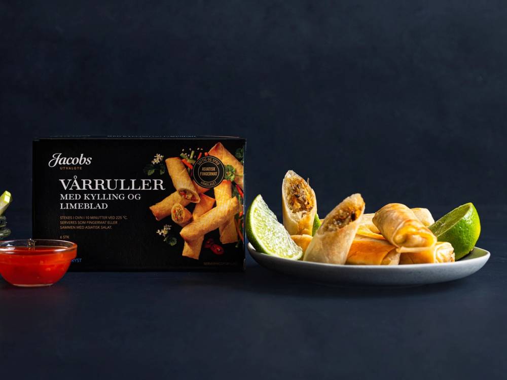 En tallerken med vårruller med kylling og limeblad, og en liten skål med saus ved siden av, mot en mørk bakgrunn.