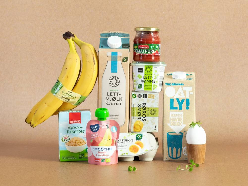 Økologiske matvarer og drikkevarer, inkludert bananer, yoghurt, juice, melk og andre produkter, på et bord.