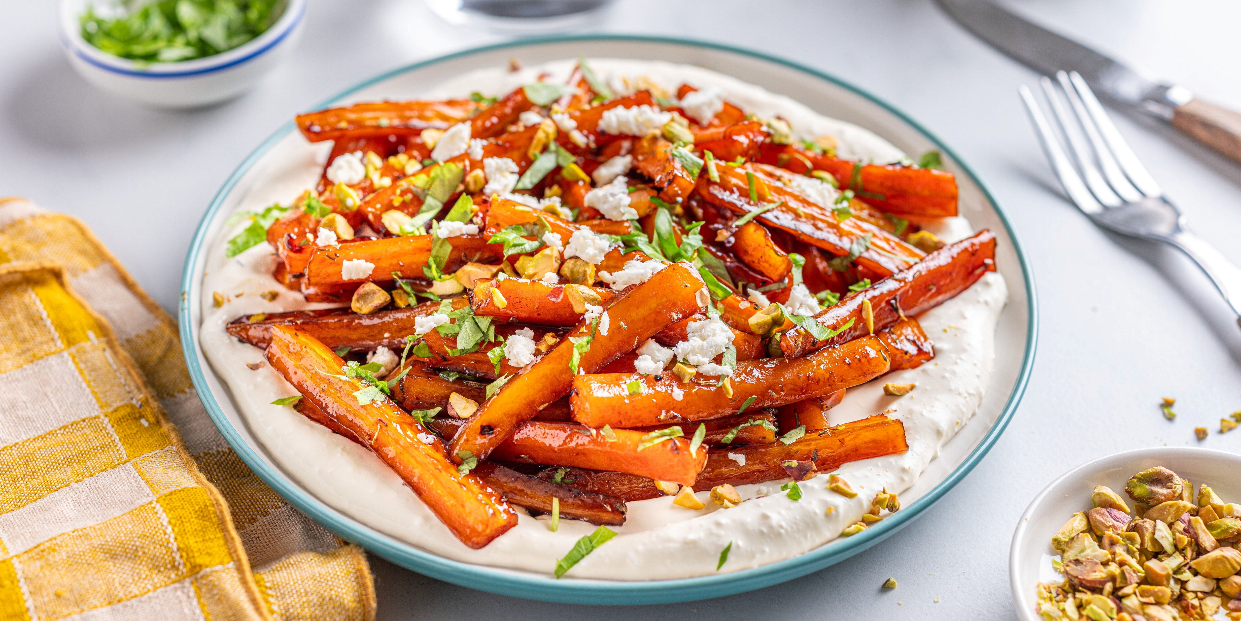 Bakte gulrøtter med honning og balsamico servert på en tallerken med hakket grønt og hvitløk, med bestikk og en serviett ved siden av.
