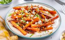 Bakte gulrøtter med honning og balsamico servert på en tallerken med hakket grønt og hvitløk, med bestikk og en serviett ved siden av.