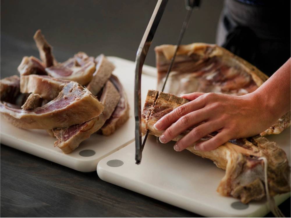 Person skjærer opp pinnekjøtt på skjærebrett før tilberedning.