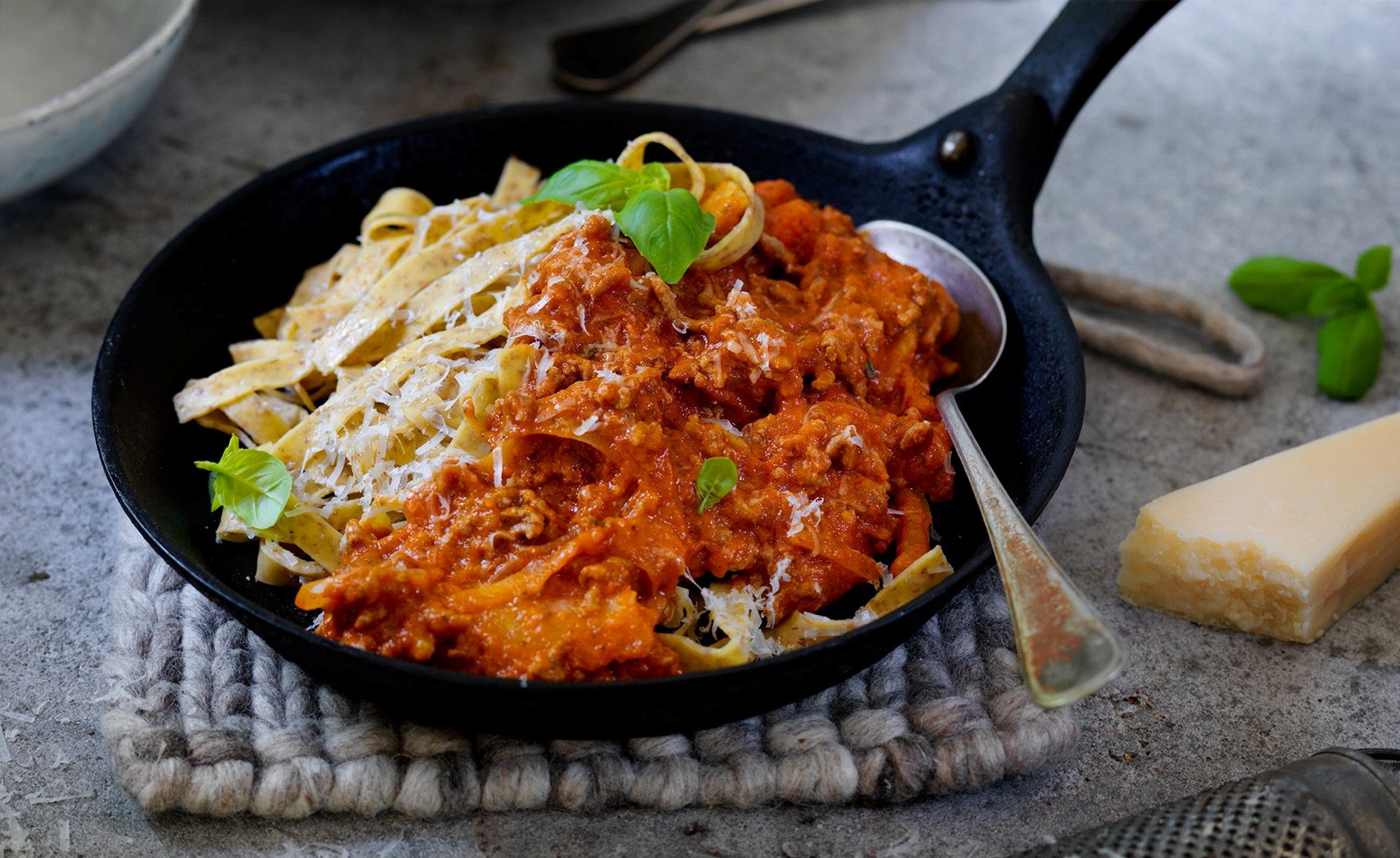 Pasta med kjøttsaus servert i en svart stekepanne, pyntet med friske urter.