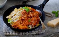 Pasta med kjøttsaus servert i en svart stekepanne, pyntet med friske urter.