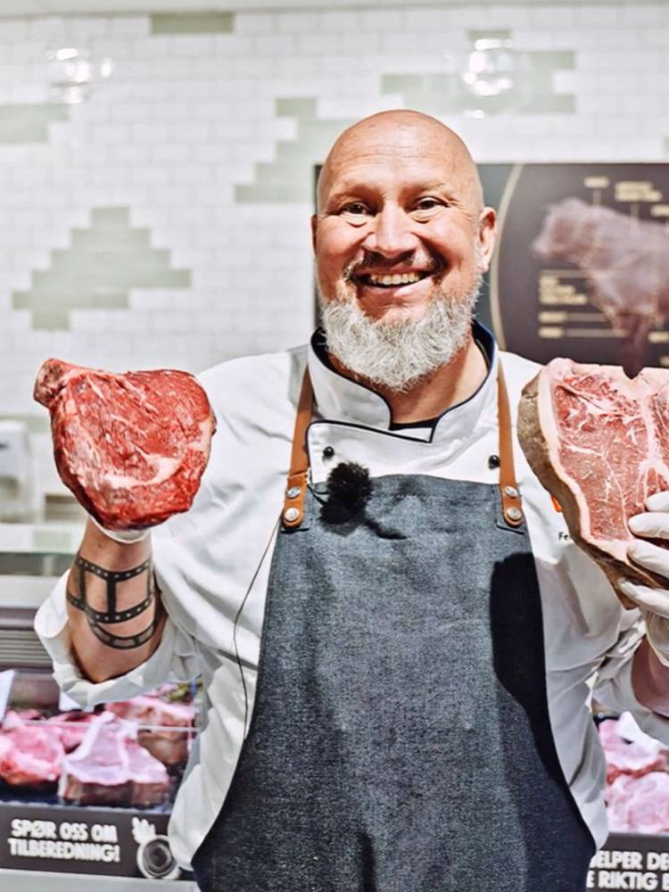 Kokk i kjøkkenet holder opp to store stykker rått kjøtt, med ansiktet dekket til for anonymitet.