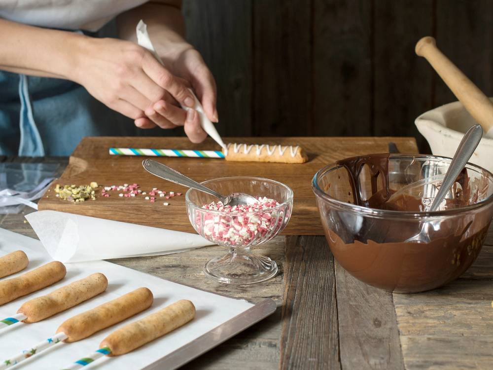 Person som pynter en kransekakestang med små sukkerperler og dekorasjoner på et kjøkkenbord.