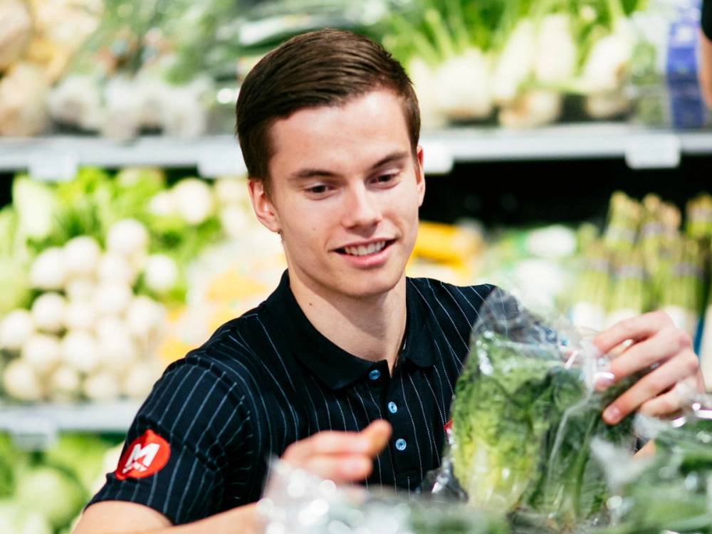 Person som handler grønnsaker i en butikk eller på marked, med blomster i bakgrunnen.
