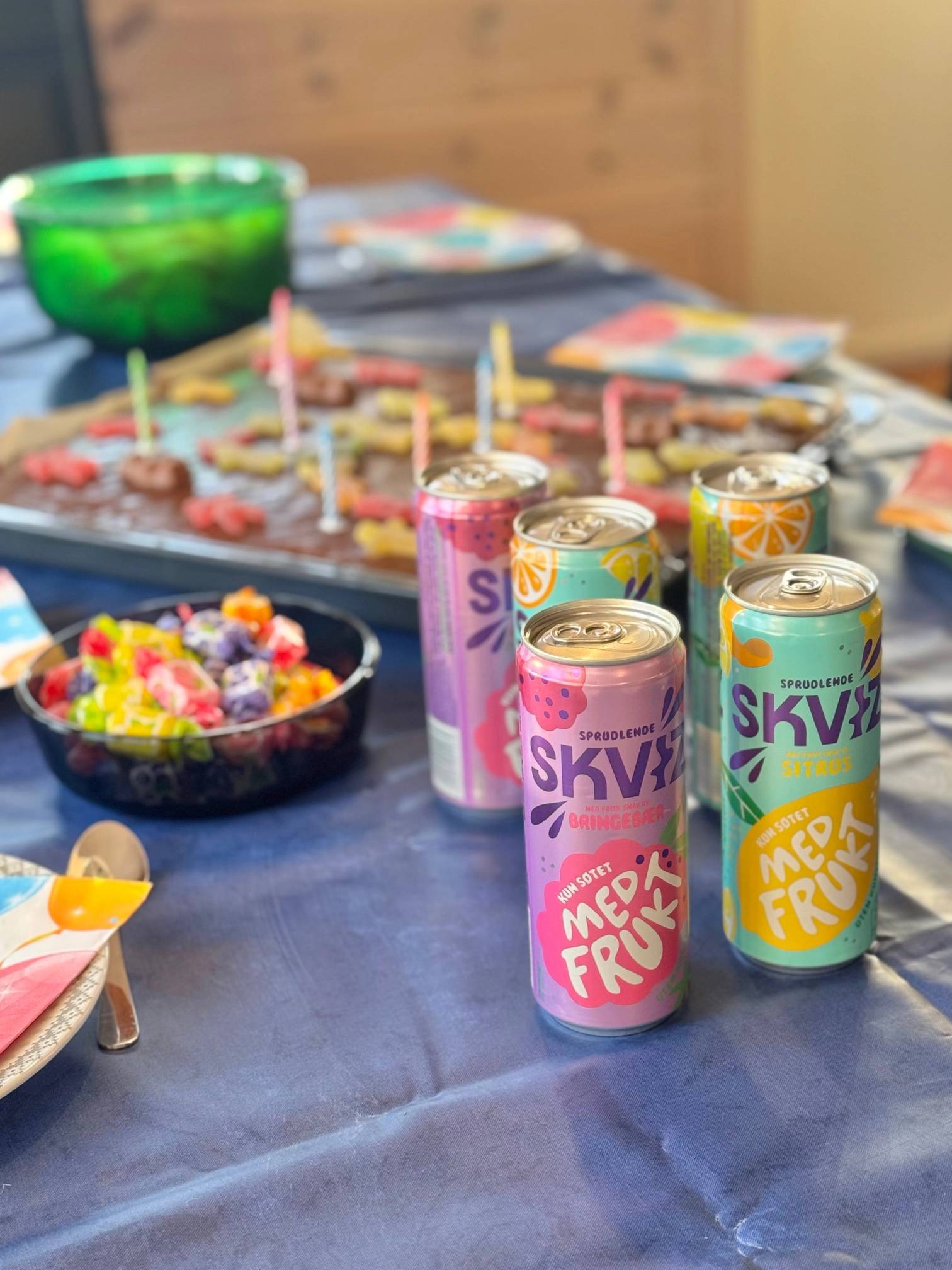 Seks bokser med SKV og Mye Frukt på en borddekkings med kaker og lys i bakgrunnen.