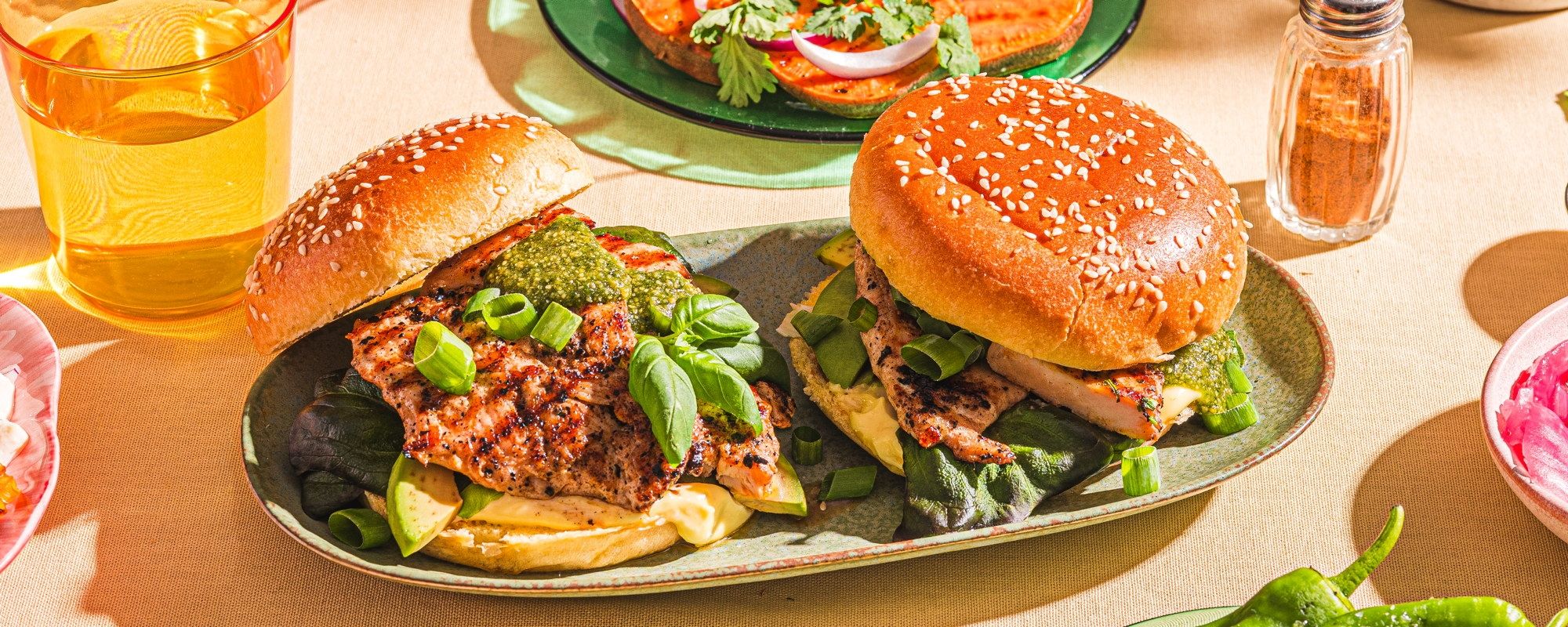 To burgere med salat og kjøttdeig på en tallerken, omgitt av tilbehør som pommes frites og grønnsaker.