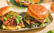 To burgere med salat og kjøttdeig på en tallerken, omgitt av tilbehør som pommes frites og grønnsaker.