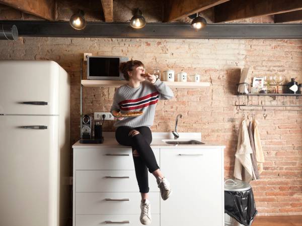 En student som drikker fra et glass på kjøkkenet, med hvite skuffer og en hvit kjøleskap i bakgrunnen.