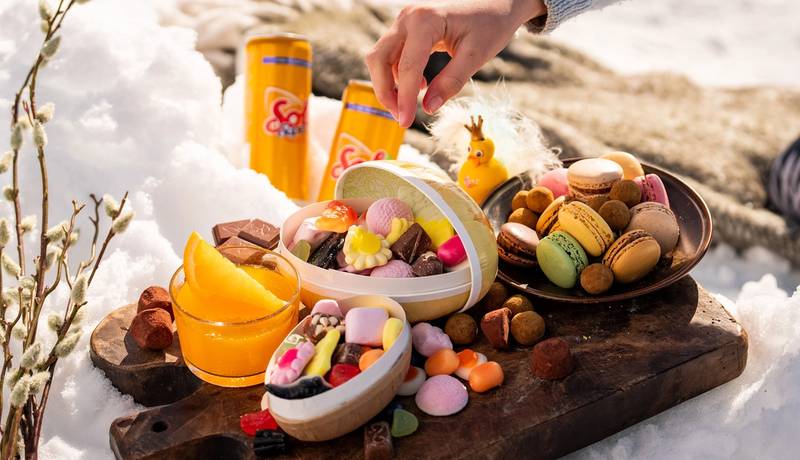 Påskegodt og påskeegg på et trebrett ute i snøen.