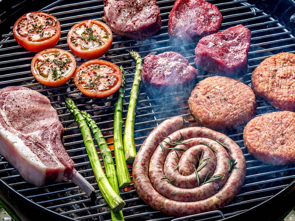 Grill med kjøtt, pølser, tomater og asparges på grillristen.