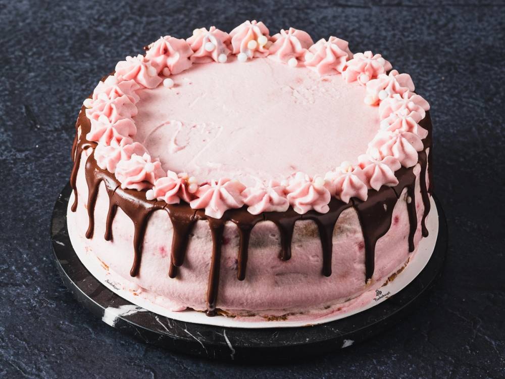 En rund kake med rosa krem og sjokoladetrekk som drypper ned på sidene, plassert på en svart overflate.