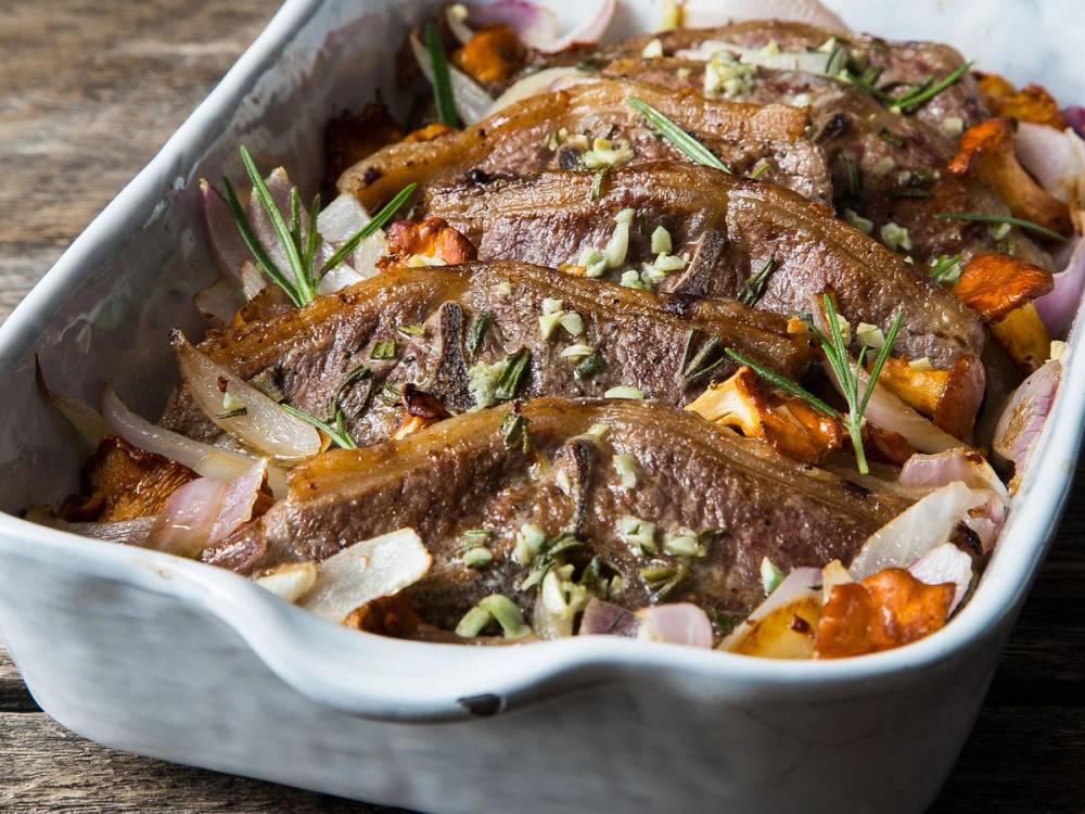 Koteletter i en ildfast form med grønnsaker og urter, klar til å bli servert.