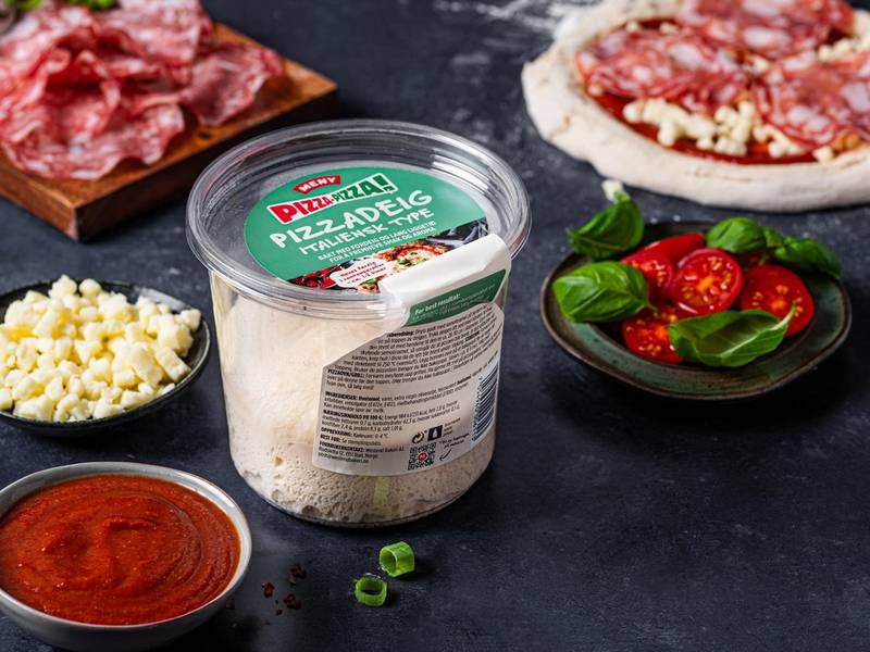 Ulike ingredienser for å lage pizza, inkludert skinke, mozzarellaost, cherrytomater og pizzasaus, er arrangert på en svart overflate.