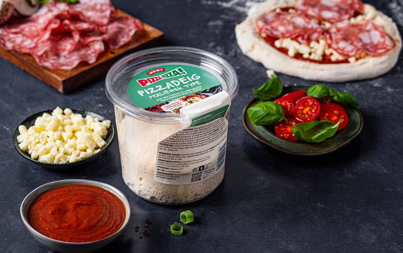 Ulike ingredienser for å lage pizza, inkludert skinke, mozzarellaost, cherrytomater og pizzasaus, er arrangert på en svart overflate.