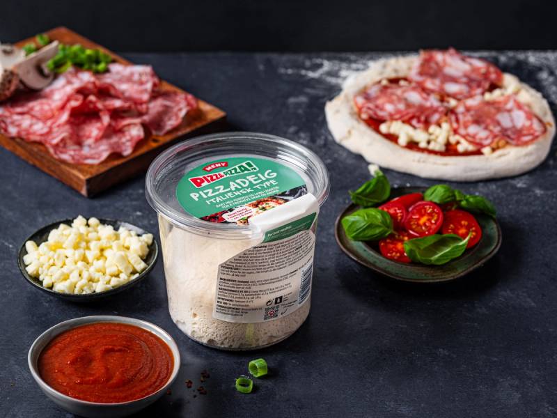 Ulike ingredienser for å lage pizza, inkludert skinke, mozzarellaost, cherrytomater og pizzasaus, er arrangert på en svart overflate.