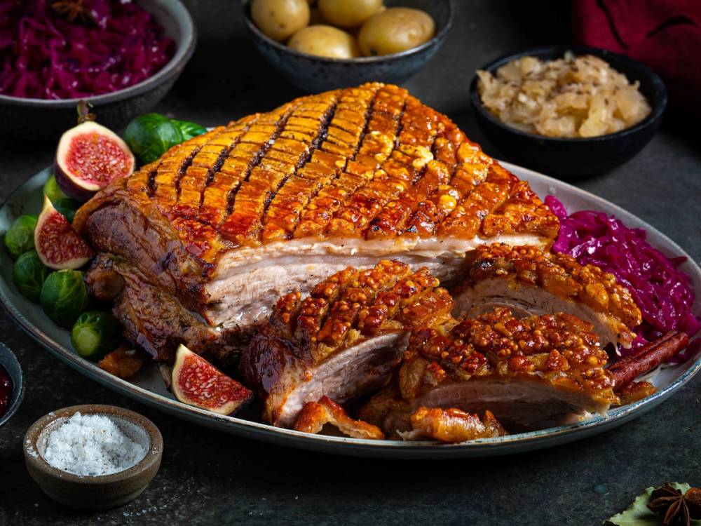 Ribbe med sprø svor, servert med tilbehør som rosenkål, poteter og surkål, på et festbord.