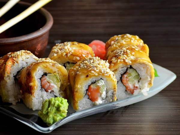 Sushi-ruller med laks, agurk og ris på en hvit serveringsplate med wasabi og ingefær ved siden av.