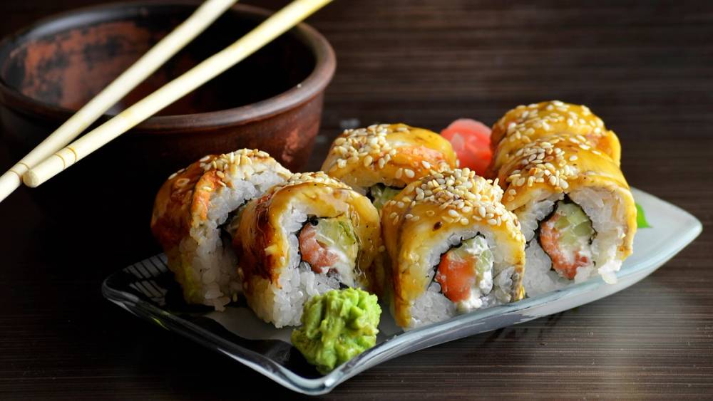 Sushi-ruller med laks, agurk og ris på en hvit serveringsplate med wasabi og ingefær ved siden av.