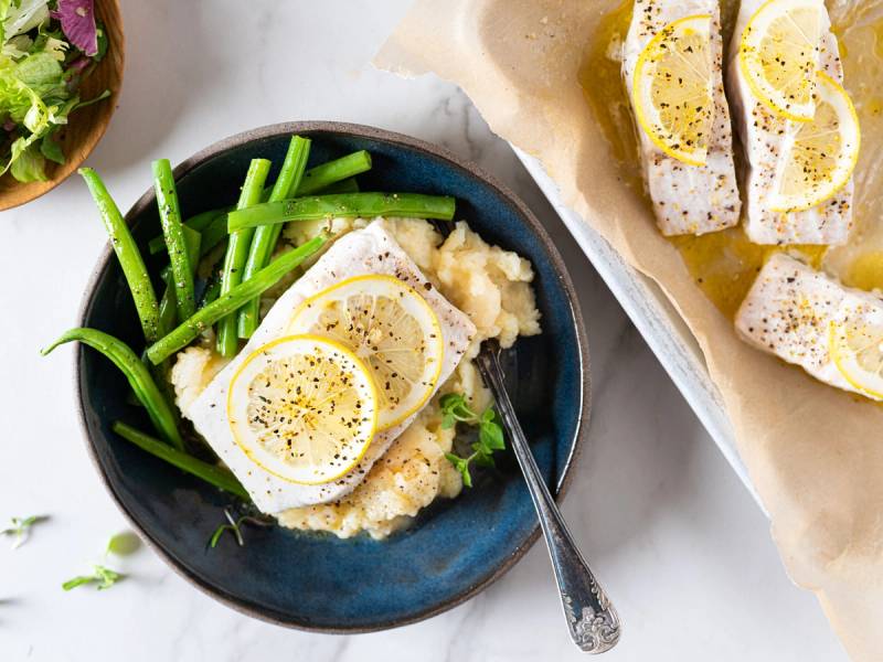 Stekt sei med sitron og grønnkål på en tallerken, med flere sitronbåter på et papir ved siden av.
