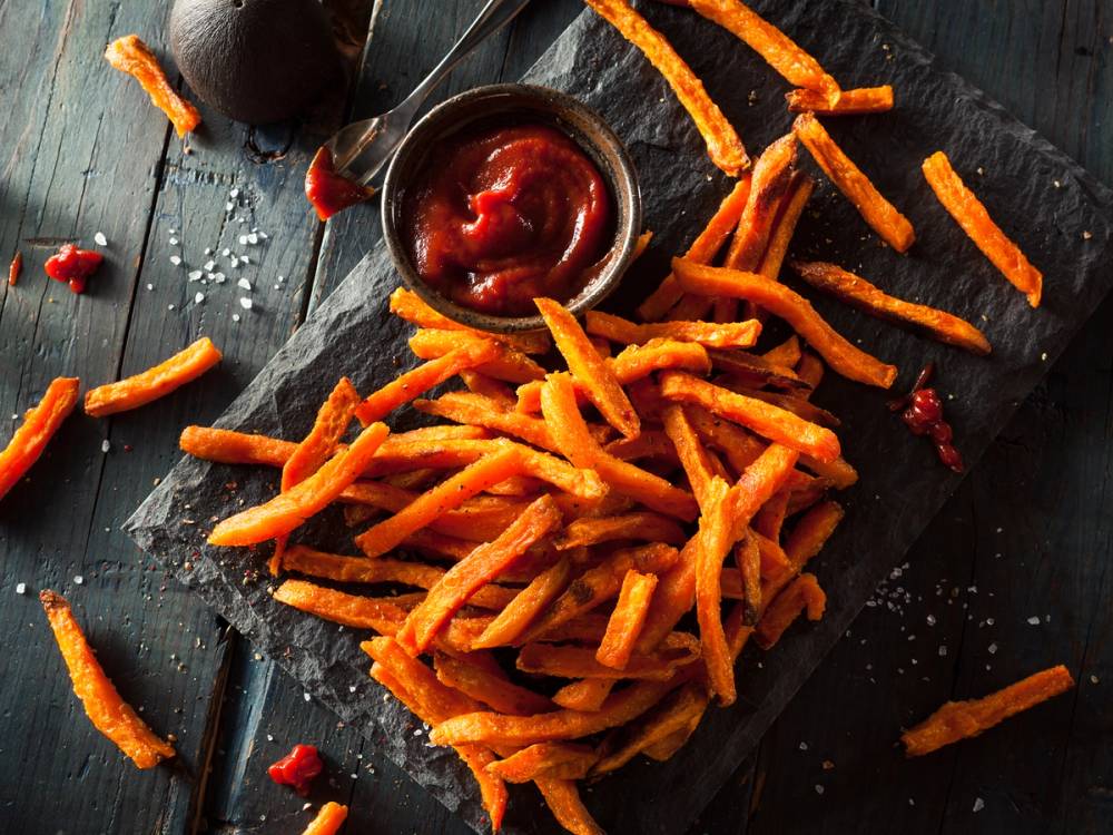 Søtpotetchips med en liten skål med ketchup på en svart stekeplate