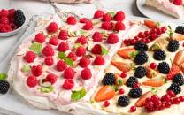 To store pavlovaer med krem og friske bær, plassert på et hvitt bord.