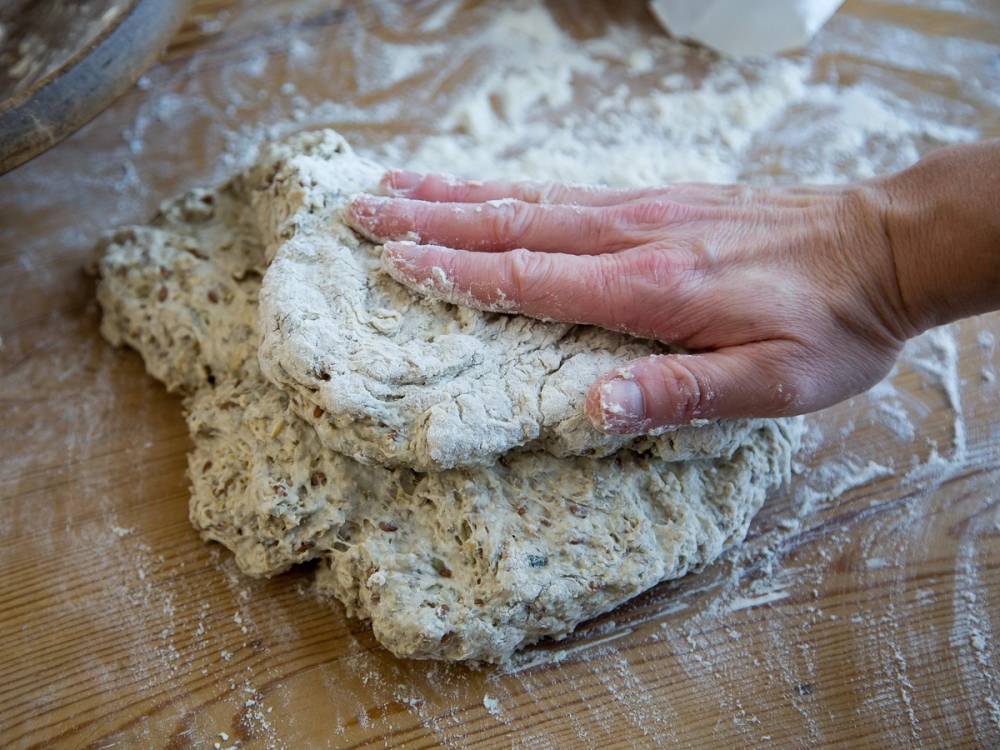 En hånd som knar deig på et melet underlag, klar for baking.