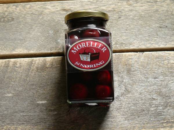 Et glass med moreller i en glasskrukke med lokk, plassert på et treverkbord.