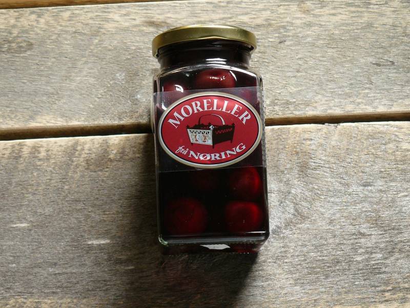 Et glass med moreller i en glasskrukke med lokk, plassert på et treverkbord.