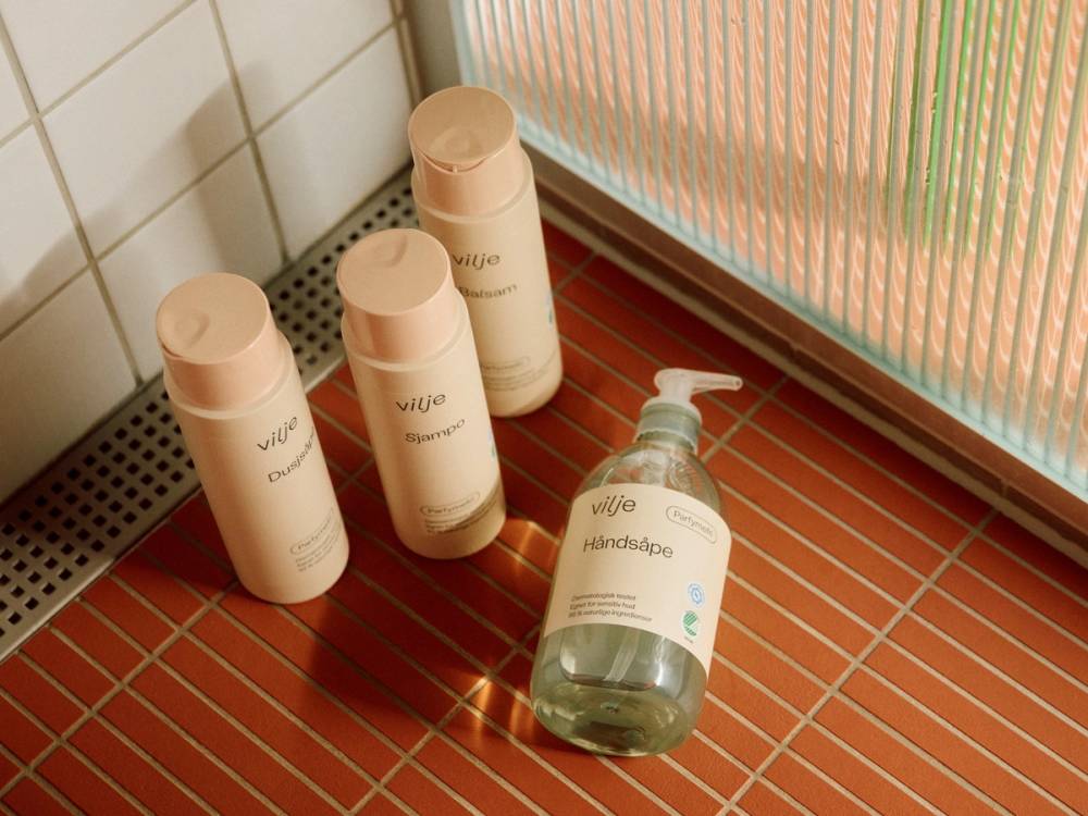 Tre hvite flasker og en hånddesinfeksjonsflaske står på et flislagt badekar på badet, med en dusjvegg i bakgrunnen.