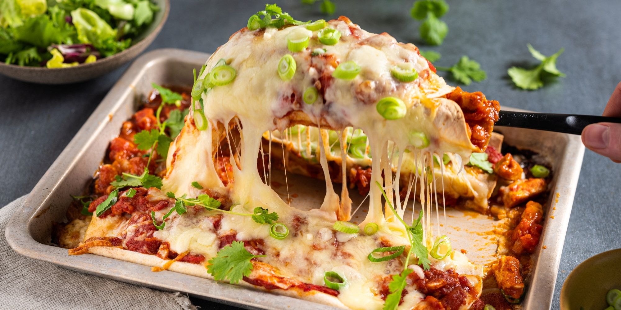 En tallerken med enchiladas fylt med kylling og smeltet ost, med grønne løk og koriander som garnityr.