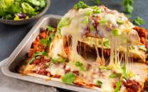 En tallerken med enchiladas fylt med kylling og smeltet ost, med grønne løk og koriander som garnityr.