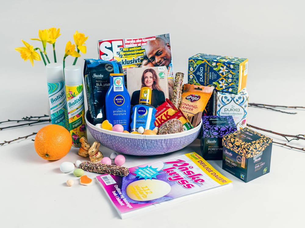 Påskeegg og ulike produkter som kremer, sjokolade og magasiner ligger i en skål og rundt den på et bord.