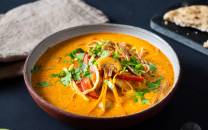 En skål med spicy grønnsaksuppe med nudler, pyntet med frisk koriander og grønnsaker, på et svart bord.