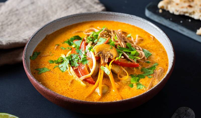 En skål med spicy grønnsaksuppe med nudler, pyntet med frisk koriander og grønnsaker, på et svart bord.