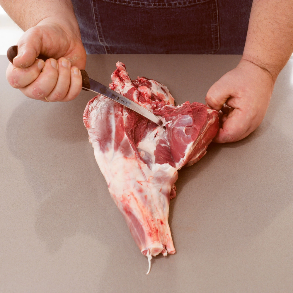 Person som skjærer i en stor kjøttbit med kniv på et kjøkkenbord.