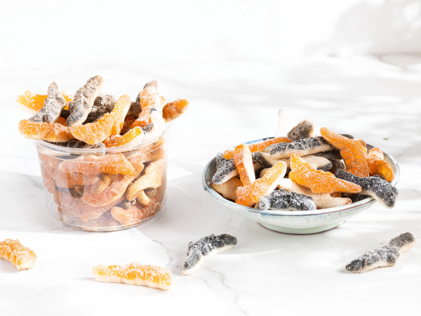 En skål og en kopp fylt med tørket frukt og gummibjørner, sannsynligvis godteri eller snacks, plassert på en hvit bakgrunn.