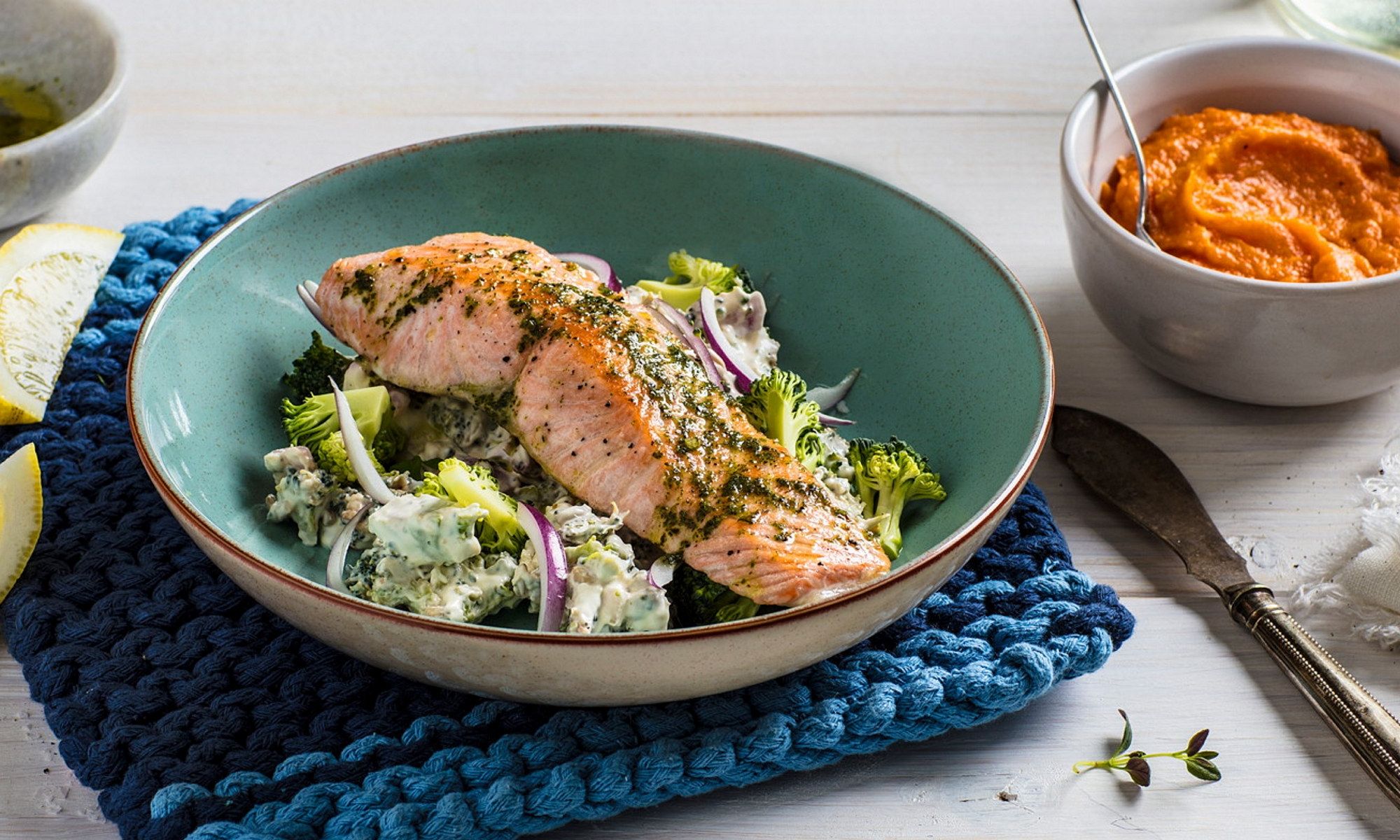 Grillet laksefilet servert på en seng av salat i en grønn bolle, med en liten skål med saus ved siden av.