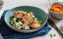 Grillet laksefilet servert på en seng av salat i en grønn bolle, med en liten skål med saus ved siden av.