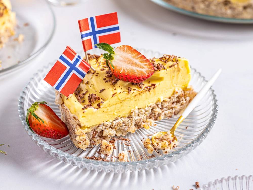 Suksessterte med jordbær og norske flagg på toppen, servert på en glassplate.