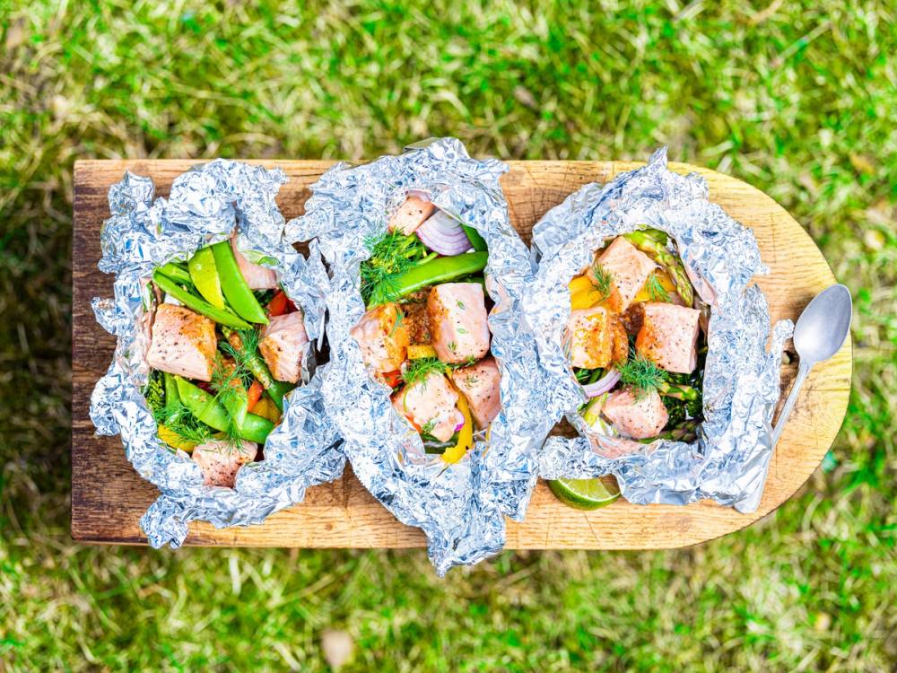 Tre åpne fiskesandwicher med salat og skiver av fisk på et trebrett, med grønt gress i bakgrunnen.