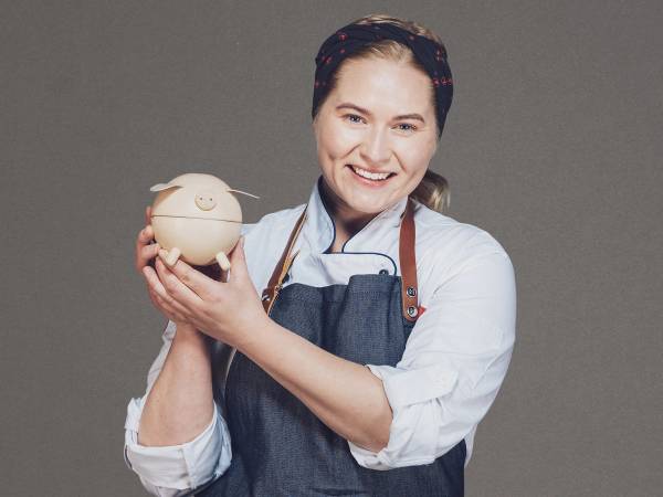 Person holder en Trumf Visa sparegris med Victoria skrevet på den, uten å vise ansiktet, mot en grå bakgrunn.