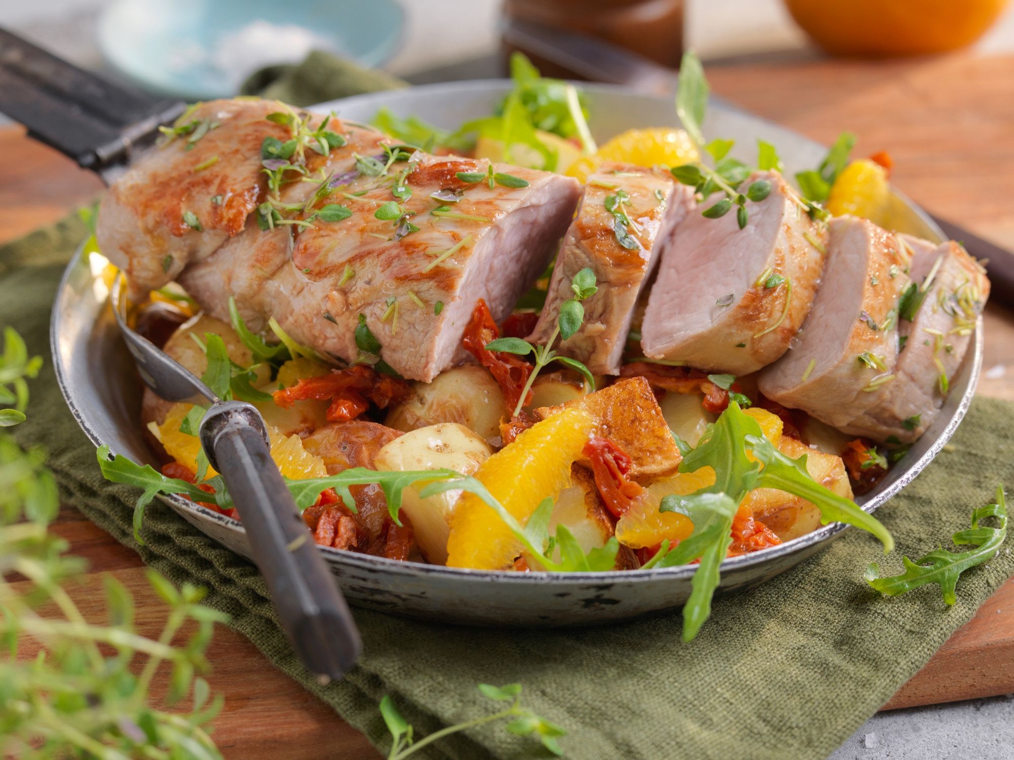 Svinefilet skåret i skiver servert på en seng av salat med sitrusbåter og urter, på en tallerken med bestikk ved siden av.