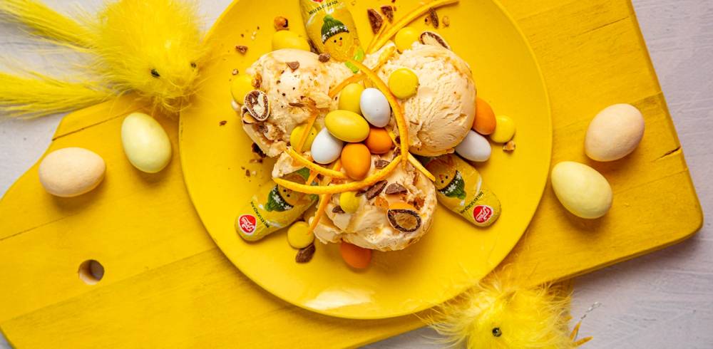 Påskekyllinger og påskeegg rundt en tallerken med kaker og godteri på et gult bord.